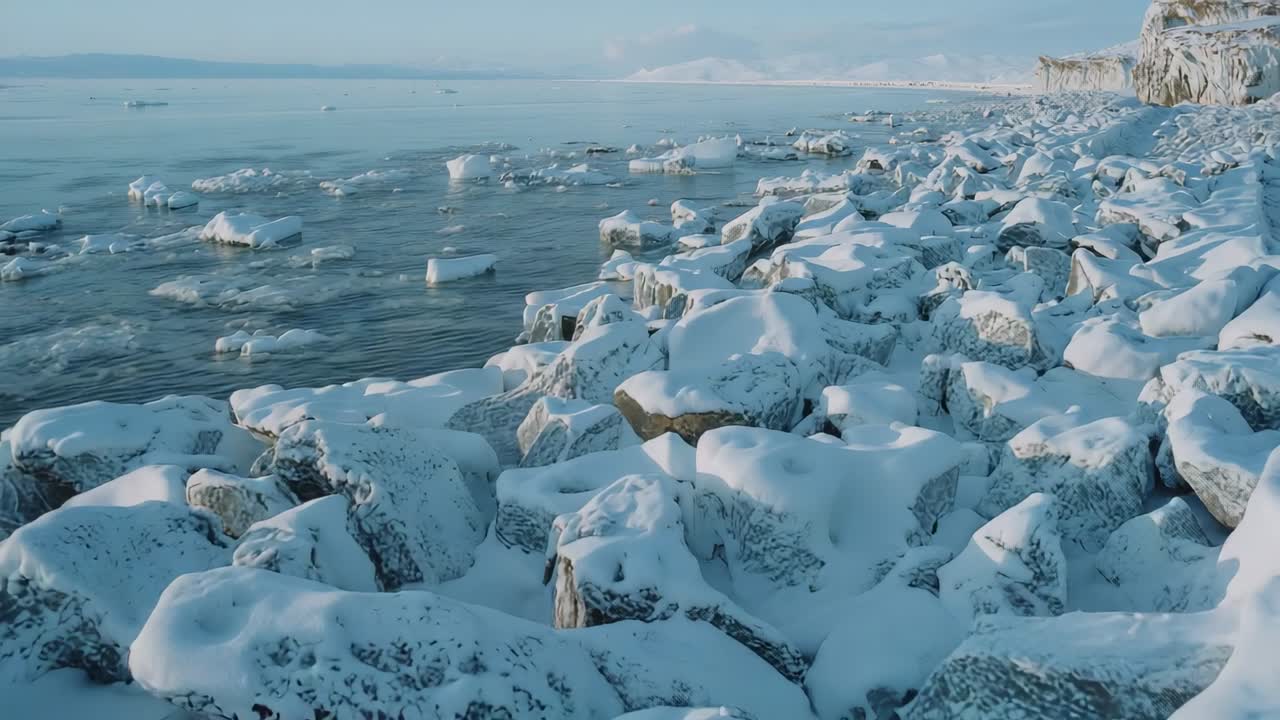 Camera initiating pan over snow-covered boulders to coastline and cliff, with ice floes drifting