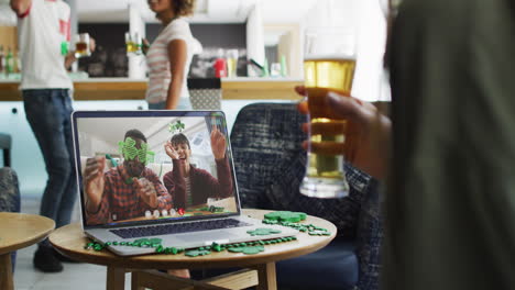 pareja sonriente y diversa que usa artículos en forma de trébol en una videollamada en una computadora portátil