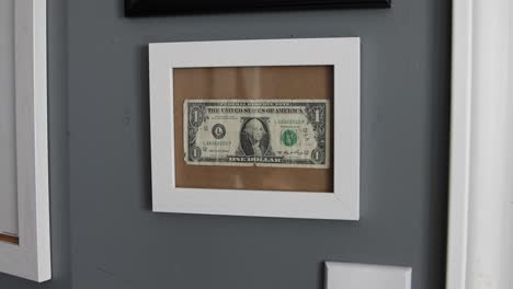 a one-dollar bill hung on a cork board with a glass front panel and white wood frame showing of financial accomplishment in somebody's bedroom