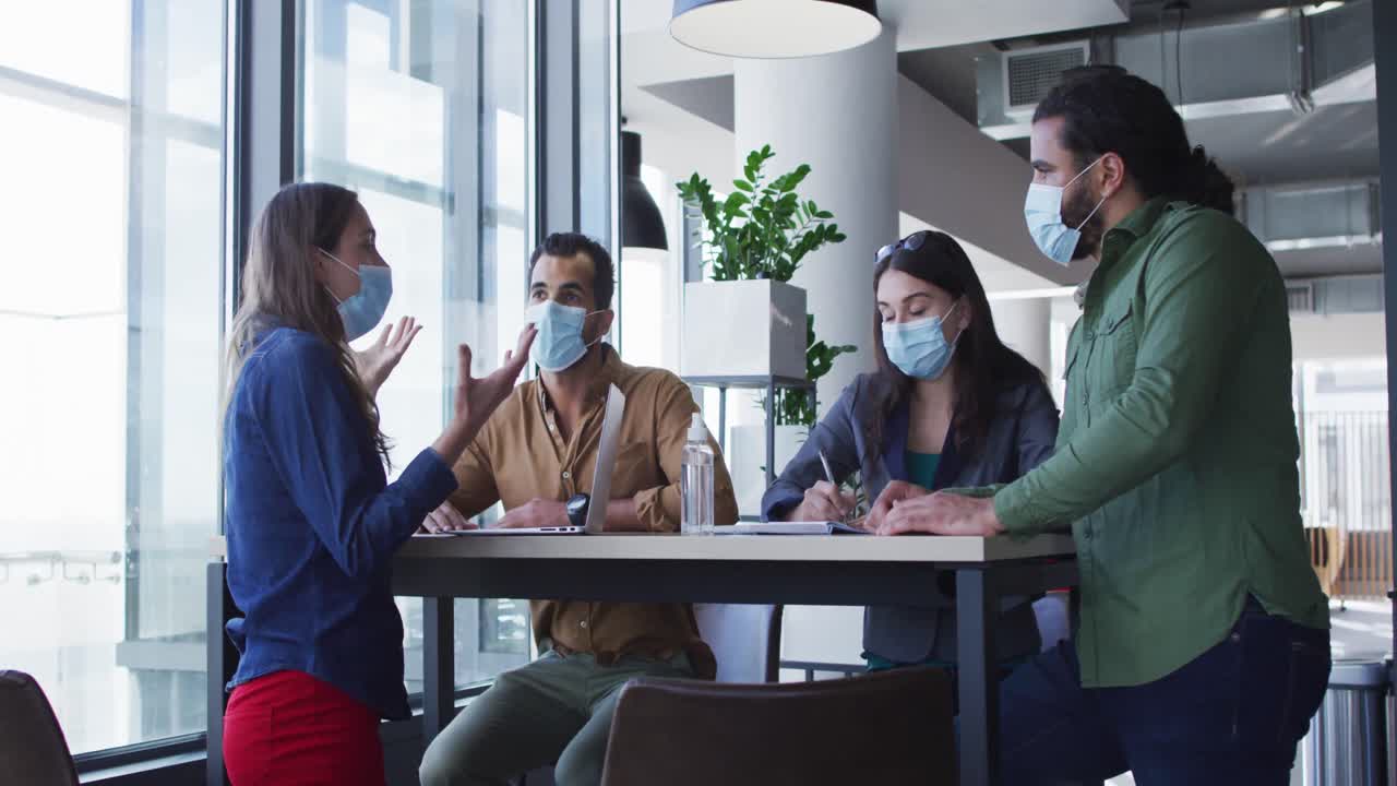 테이블 에 앉아 이야기 하는 얼굴 마스크 를 착용 한 다양한 사업 동료 들 의 그룹