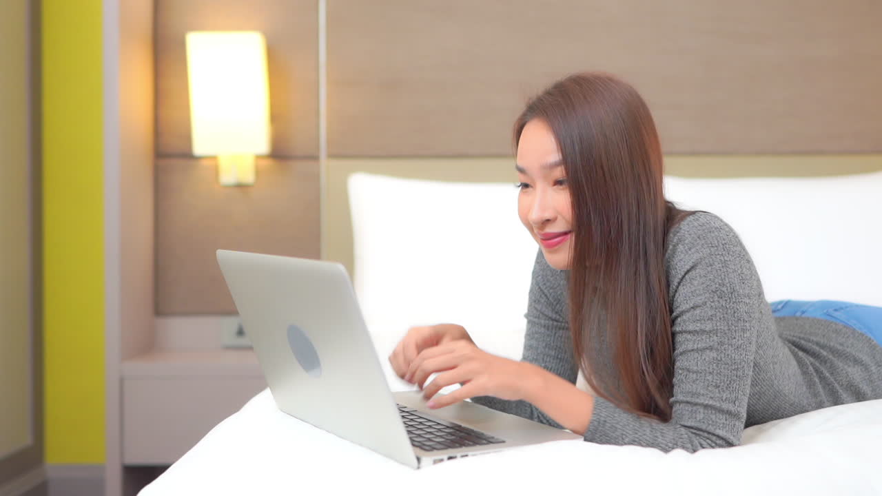 침대 펌프 주먹과 소리에 누워있는 동안 노트북을 사용하여 매력적인 아시아 여성의 슬로우 모션보기