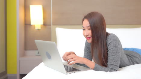 slow motion view of attractive asian woman using laptop while lying on bed pumps fists and shouts