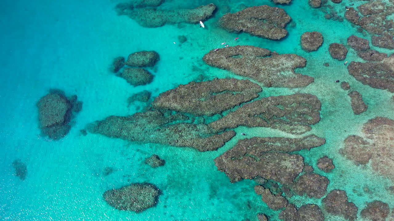 Cinematic drone tracking shot over tropical reef with vivid turquoise water, a few snorkelers and Paddle boards visible