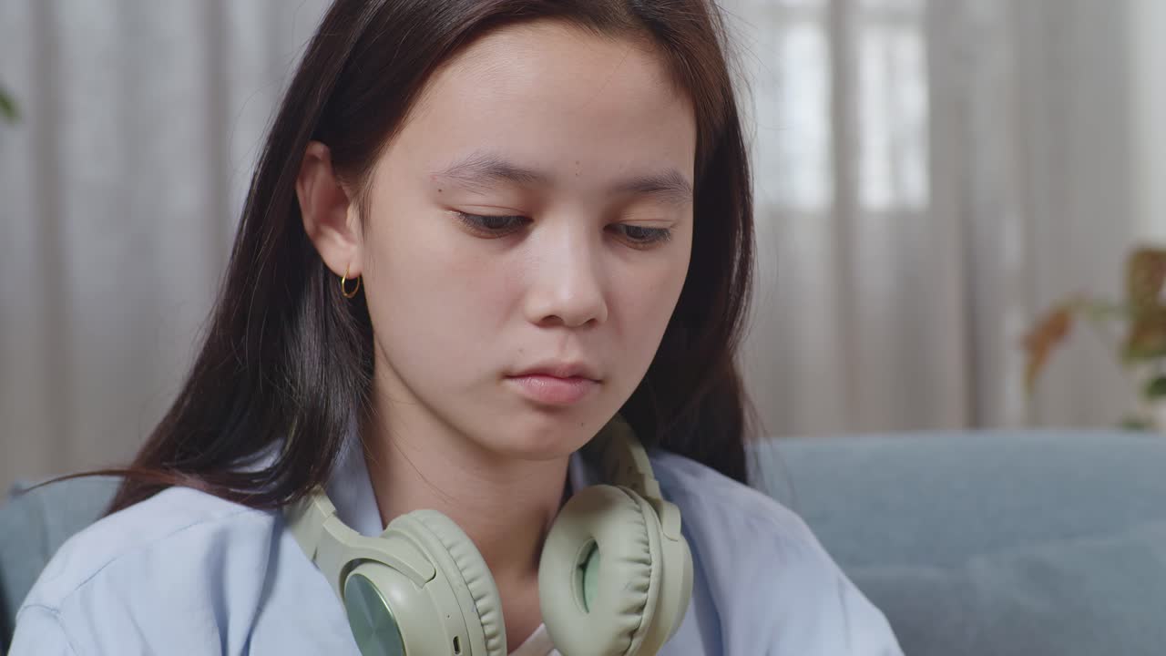 집 의 거실 의 소파 에 앉아 스마트폰 을 사용 하는 지루 한 아시아 청소년 소녀 의 근접 사진