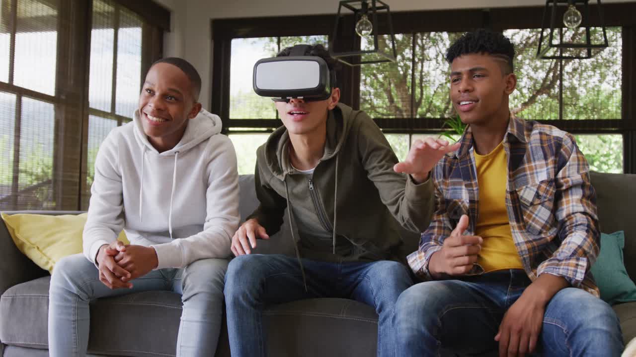 Happy diverse male teenage friends playing video games and using vr headset at home, slow motion