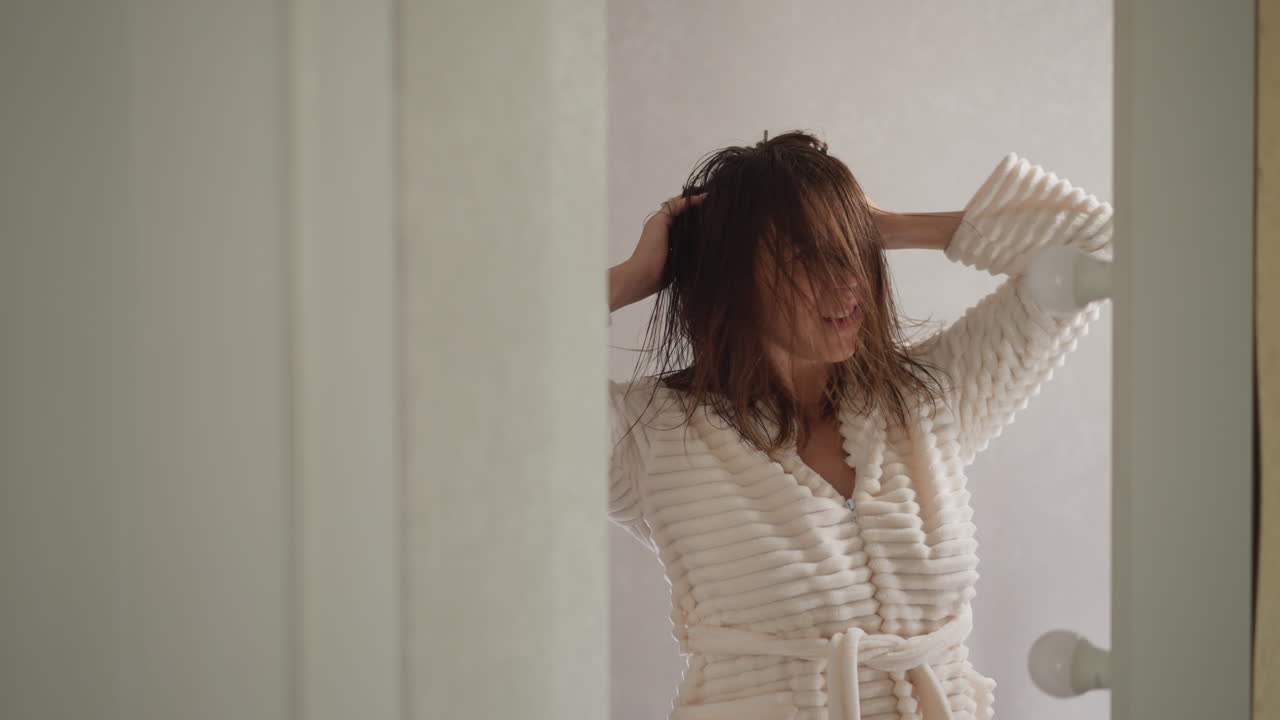 여성은 화장실에서 헤어드라이어 없이 은 머리카락을 건조시니다. 매력적인 갈색 여성은 샤워를 한 후 은머리를 곧게하는 음악을 듣고 있습니다.