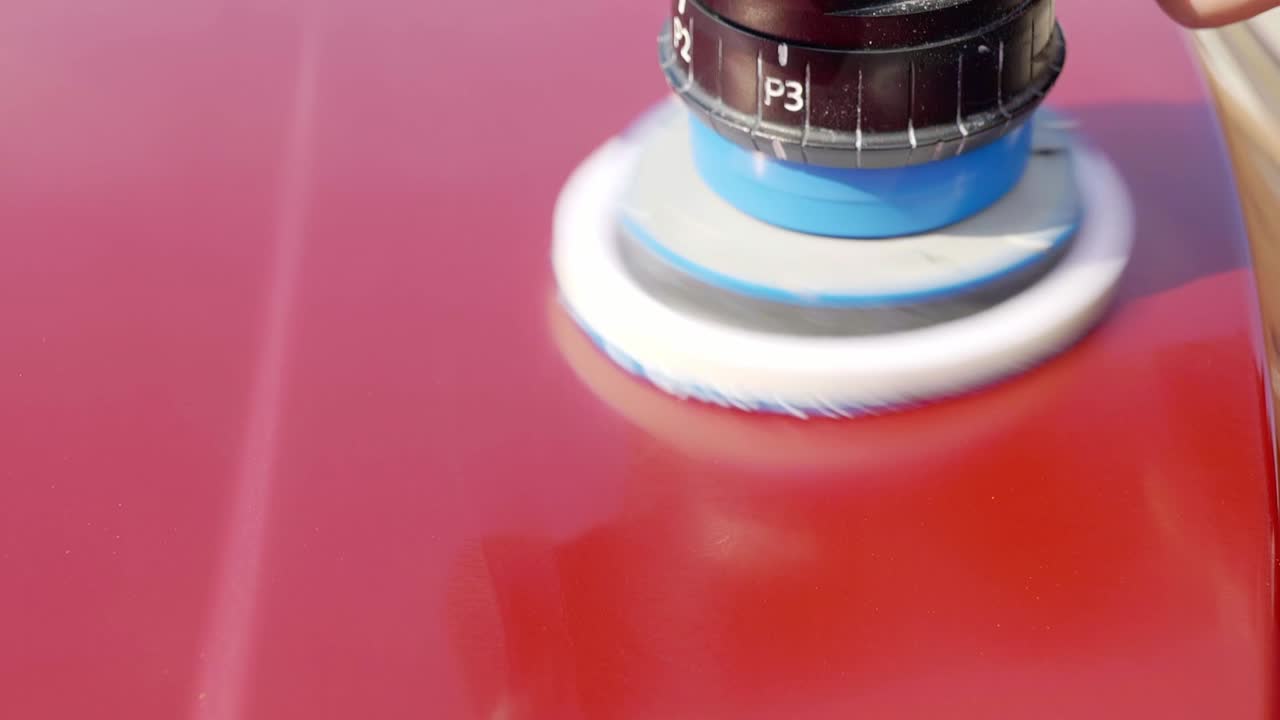 Polishing cherry red car bonnet hood with dual action machine polisher - close up