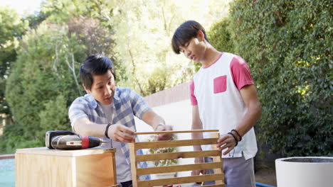 Asian father and teenage son building wooden furniture together outdoors