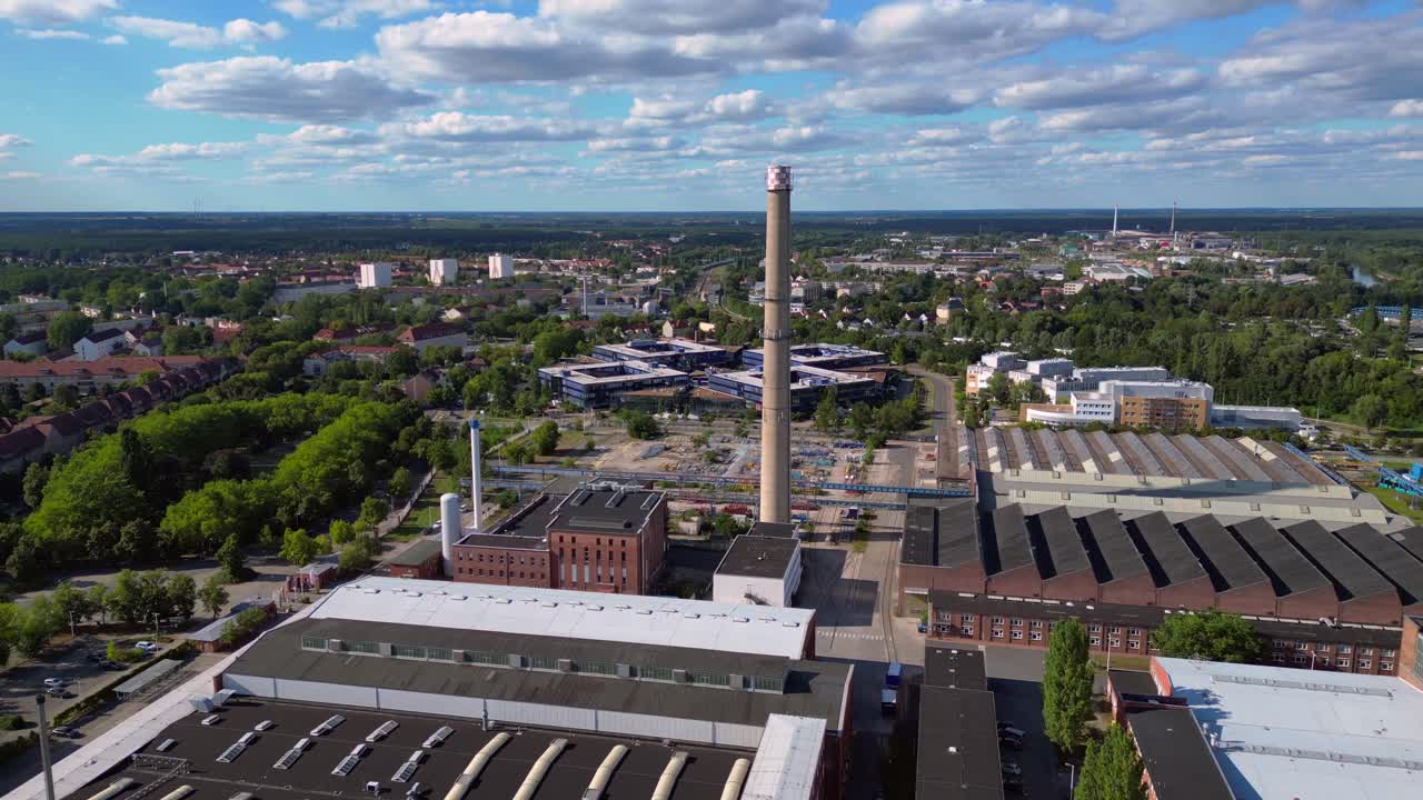 industrial buildings and a chimney in Hennigsdorf, Germany, with a train passing by. Marvelous aerial view flight pull in drone