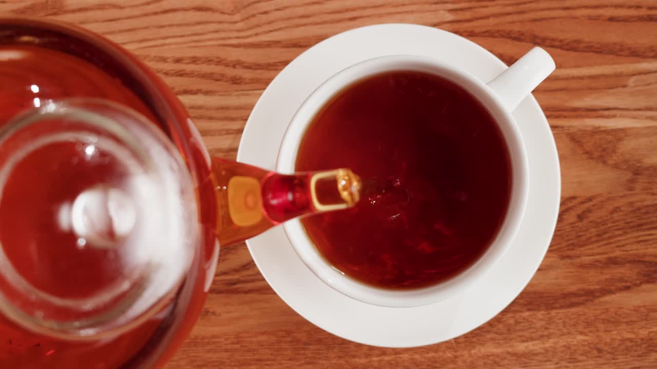 Pouring hot tea from a teapot into a white teacup