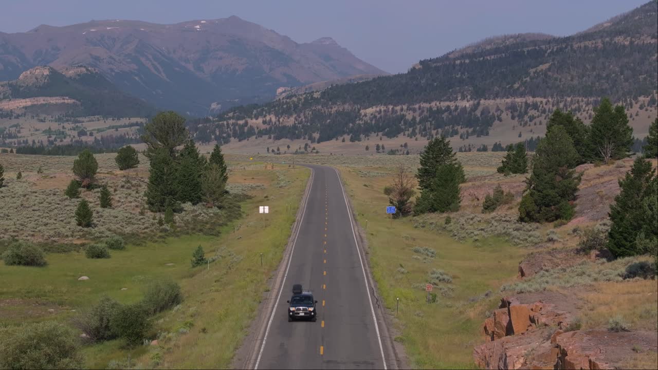 Car driving along a scenic mountain road in Wyoming, surrounded by vast open landscapes