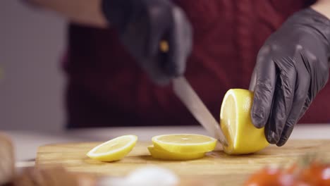 slow-motion close-up of a chef slicing a fresh lemon on a wooden board. the sharp knife cuts smoothly, revealing juicy texture. black gloves ensure hygiene, with blurred tomatoes and herbs in view