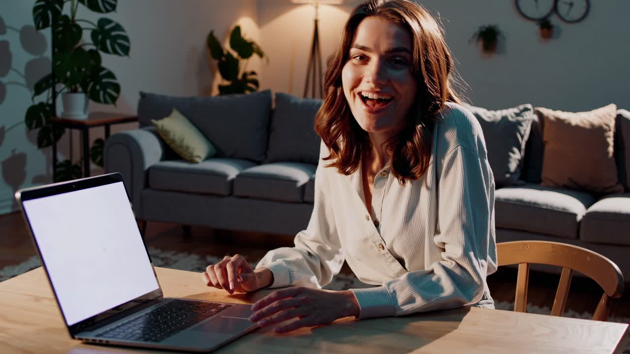 Eine Frau, die in einem gemütlichen Wohnzimmer einen Laptop anlächelt, aus einer frontalen Perspektive aufgenommen