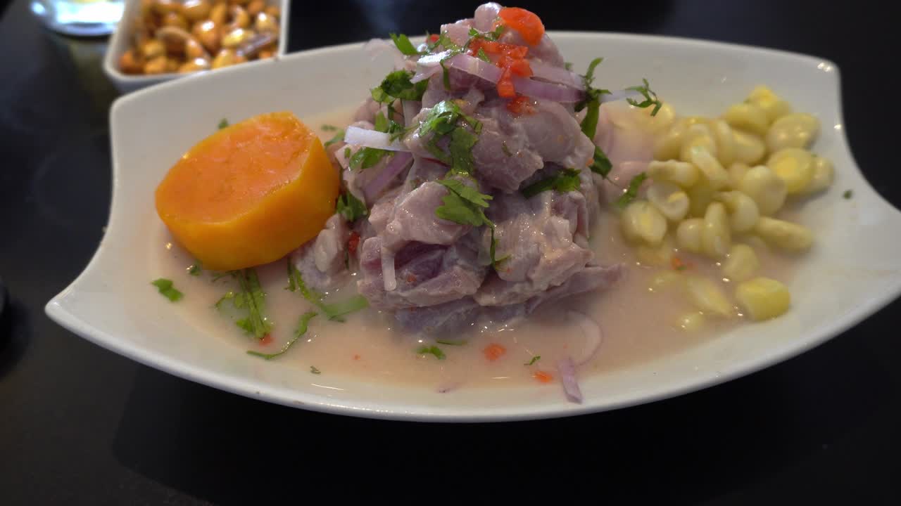primer plano de un plato de ceviche con maíz, patata dulce y canchita cerrana en una mesa negra en un restaurante