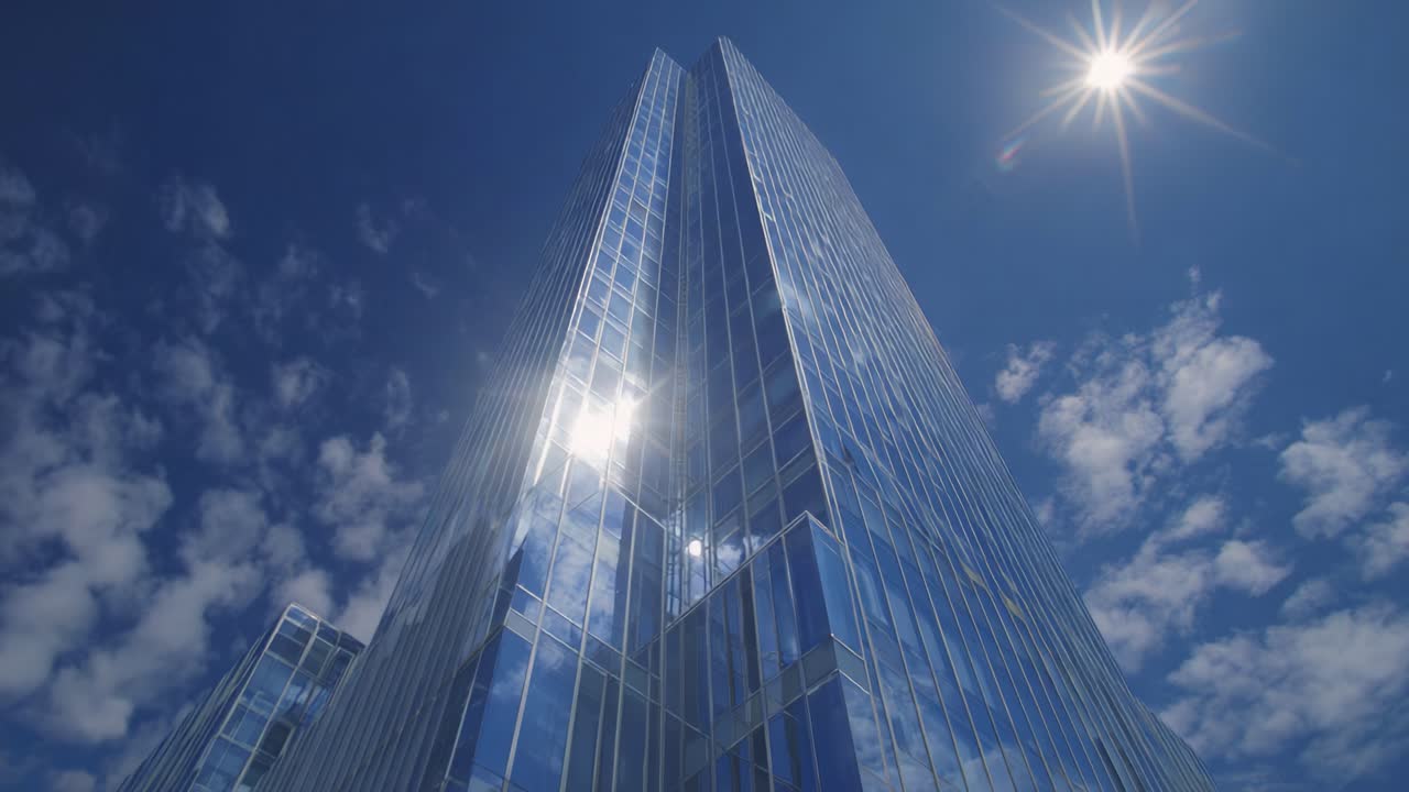 Splendido riflesso di architettura urbana sotto un cielo azzurro brillante, che mostra imponenti grattacieli di vetro con la luce del sole splendente e nuvole bianche e soffici.