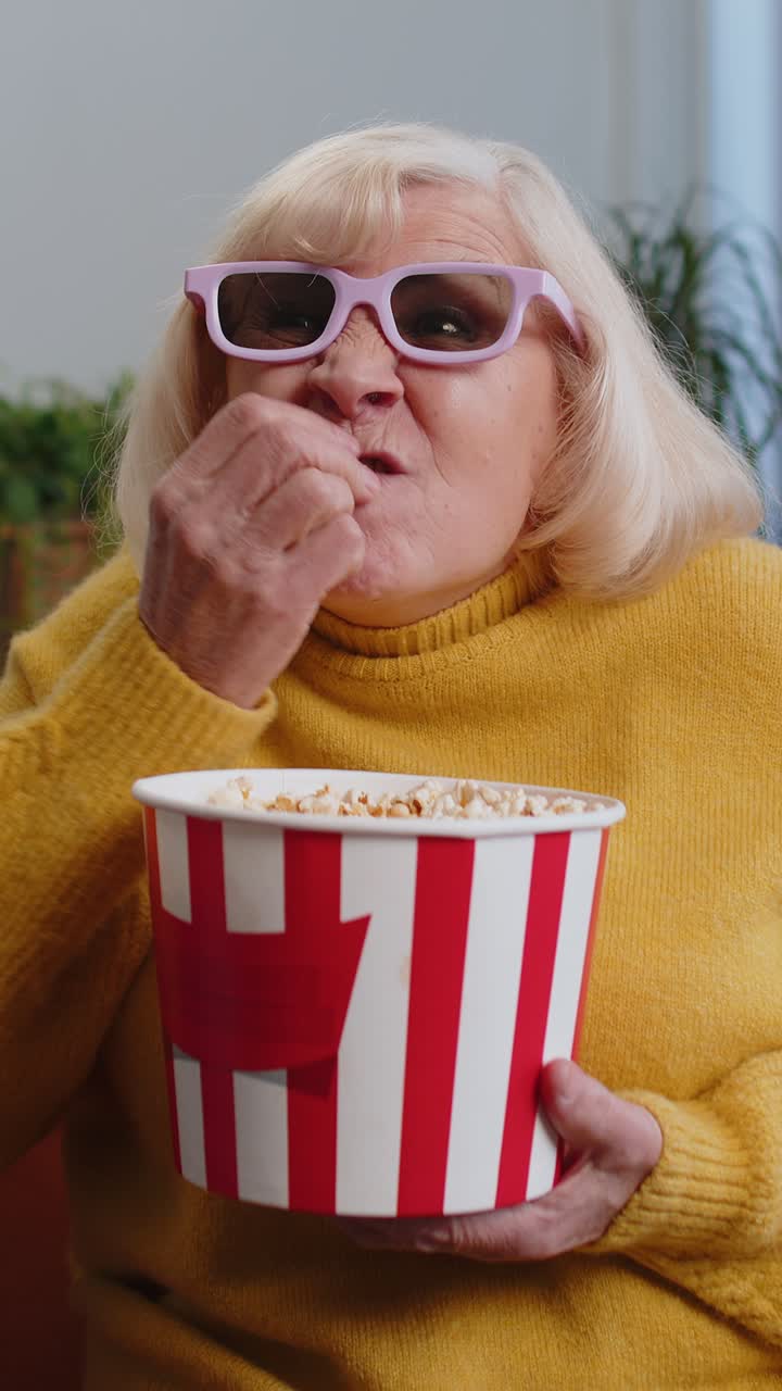 Grandmother woman on sofa eating popcorn watching interesting tv serial sport game online at home