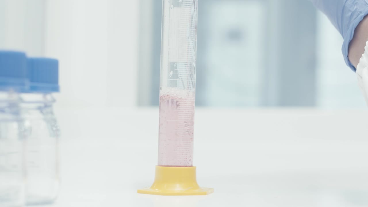 Worker Lab's hand pouring serum liquid into Measuring Tube while working in Medical Drug Production