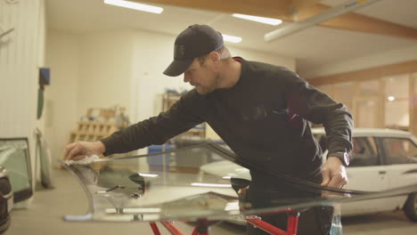 repairman in workshop use cloth to wipe clean new windshield to be installed