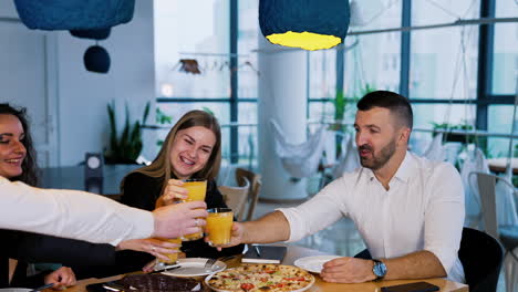 happy smiling young people clink glasses with juice sitting at table. company of friends came to have some pizza together.
