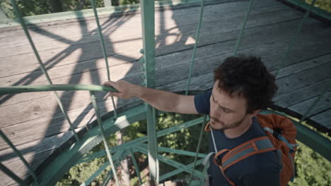 man walkig upstairs on a spiral stairway with an orange backpack to reach top of a lookout tower