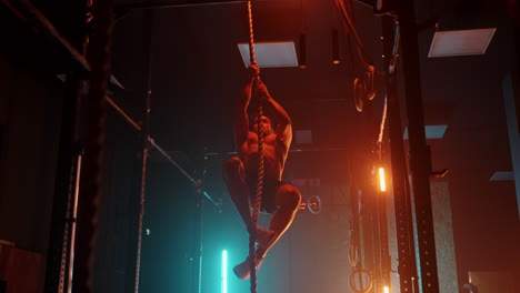 hombre de fitness haciendo ejercicio de escalada de cuerda en el gimnasio cámara lenta. luz de neón azul naranja. hombre trabajando en un gimnasio subiendo una cuerda