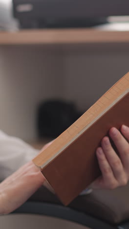 libro en manos de una joven lectora de primer plano. mujer se sumerge en la lectura girando pensativamente la página del libro en el almacenamiento de libros circundante. mujer con novela iluminada