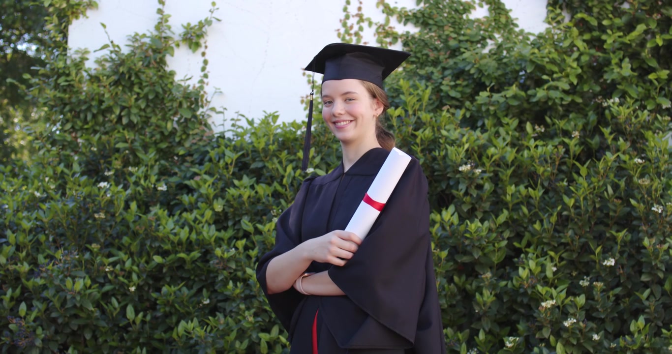 Donna che tiene in mano un tocco e un diploma con nastro rosso, si gira e sorride mentre la fotocamera si avvicina in giardino.