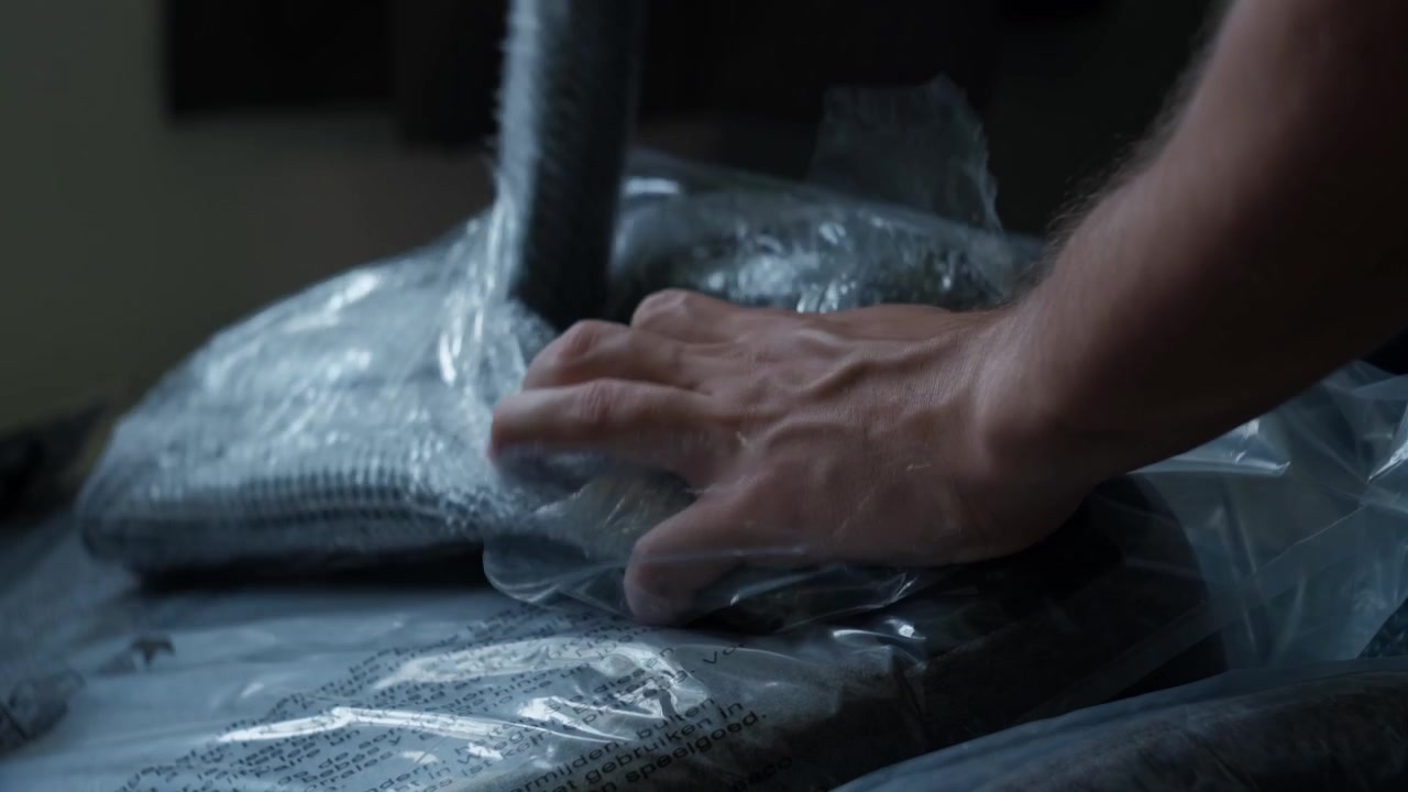 Close-up static shot of hands ripping open plastic packaging from chair parts during indoor furniture assembly