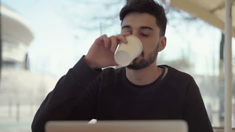 serious freelancer working with laptop and drinking coffee to go