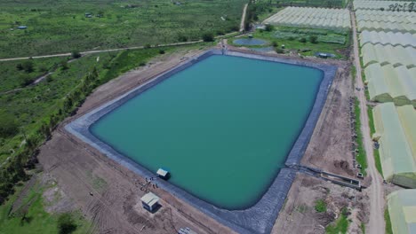 artificial reservoir with lining next to greenhouse sheds