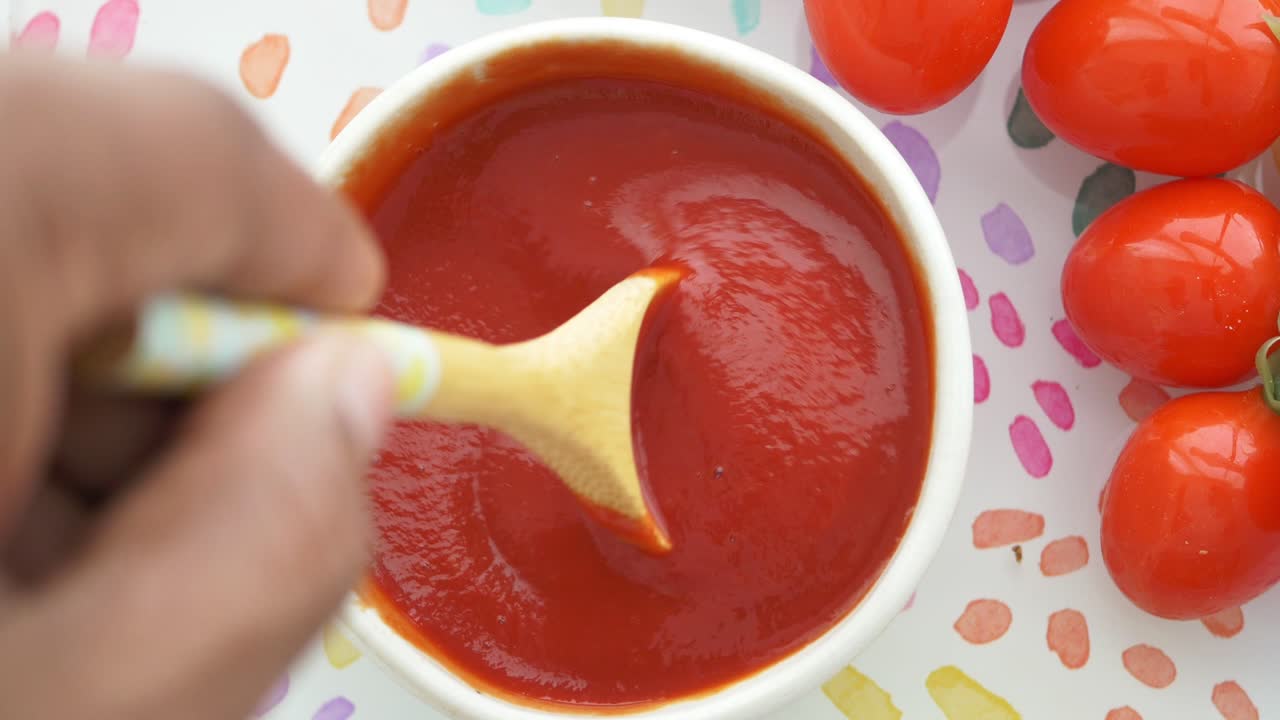 Mano che mescola ketchup di pomodoro rosso in una ciotola bianca con pomodori freschi.