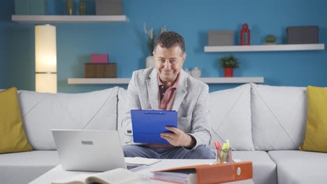 Home-office-worker-man-smiling-at-camera-looking-at-paperwork.