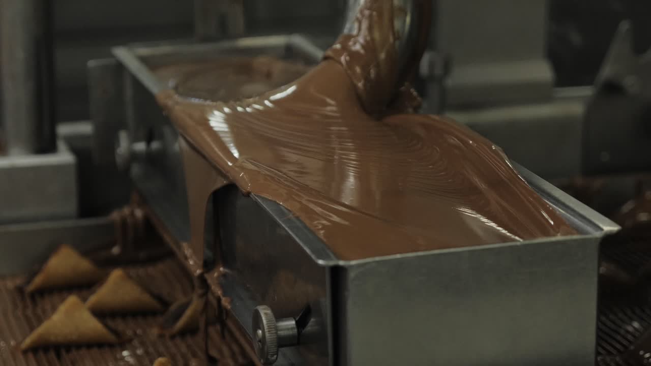 Close-up of thick melted chocolate cascading from enrober over triangular pralines on conveyor