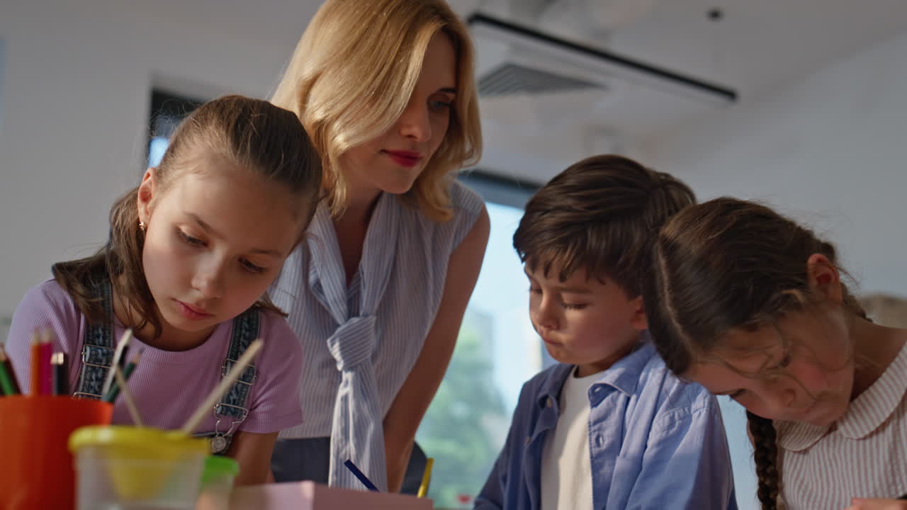 Woman teacher guiding art lesson in primary school. Young lady helping pupils