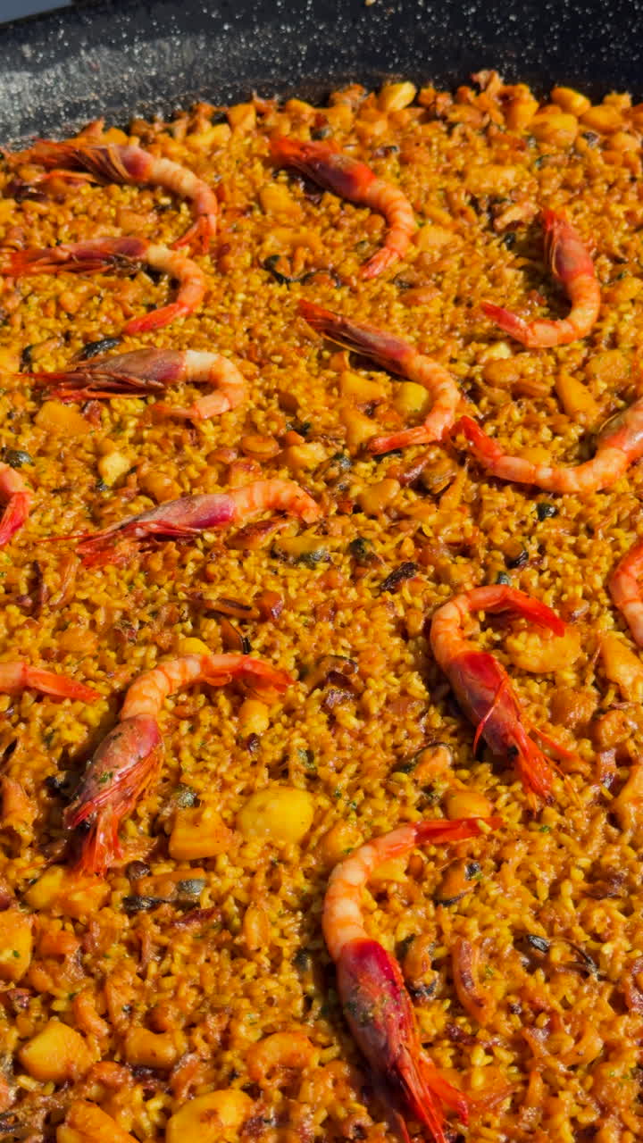 Seafood paella simmering in a large pan. Fresh prawns and rice cooking in a traditional spanish senyoret recipe with a rich golden color