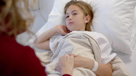 caucasian mother holding hand of tired daughter patient lying in hospital bed, slow motion