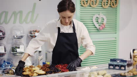 A-female-confectioner-in-a-black-apron-in-a-grocery-store-arranges-cakes-on-a-showcase