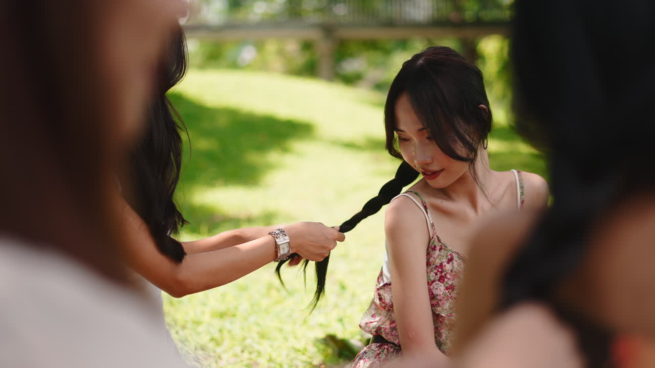 公園で友人に髪を編んでもらっている若いアジア人女性