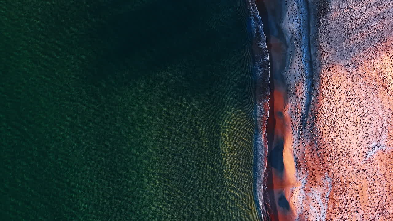 Paesaggio acquatico con superficie increspata e onde che si infrangono sulla riva. Spiaggia sabbiosa coperta da numerose orme. Vista dall'alto