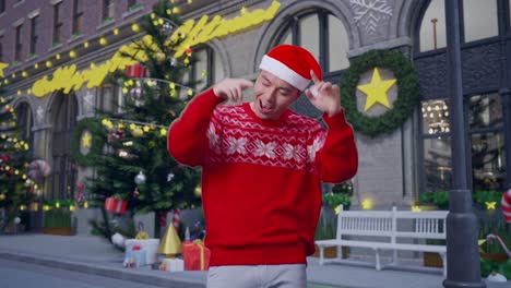 cheerful asian man in santa suit dancing while standing in christmas night