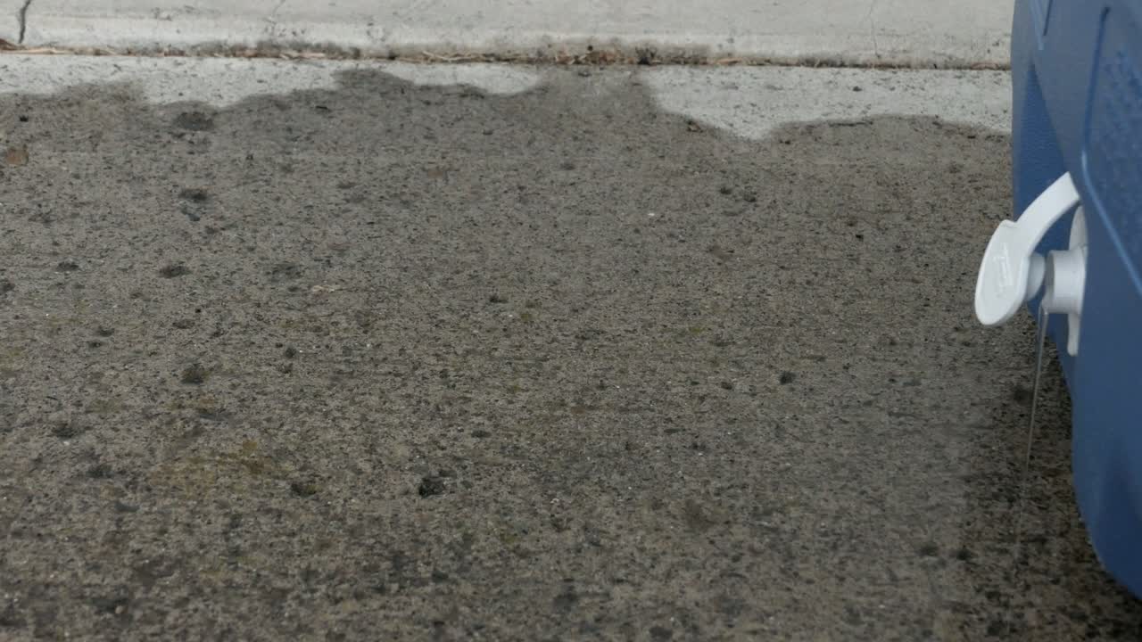 Blue cooler drain out the last of the water from the melted ice onto a concrete pad