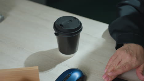 close up of lady placing takeaway tea cup on wooden office desk beside computer, setting up workspace for focused morning routine in calm office environment with soft shadows and natural light