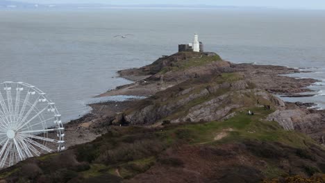 drone view capturing the big wheel near mumbles pier swansea with rocky hills and mumbles lighthouse at background in england.