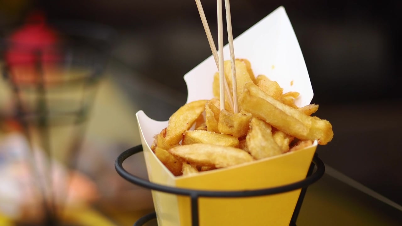 Närbild på krispiga pommes frites i en gul pappersstrut.