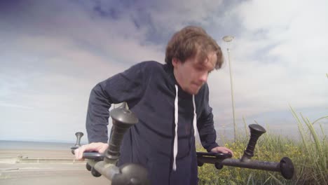 young male struggles to do his reps on outdoor push up bars in sunny weather