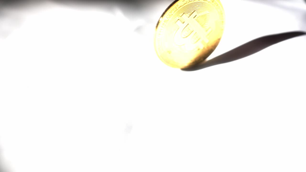 mano girando bitcoin de oro macizo hasta que se detiene y cae plano sobre fondo blanco