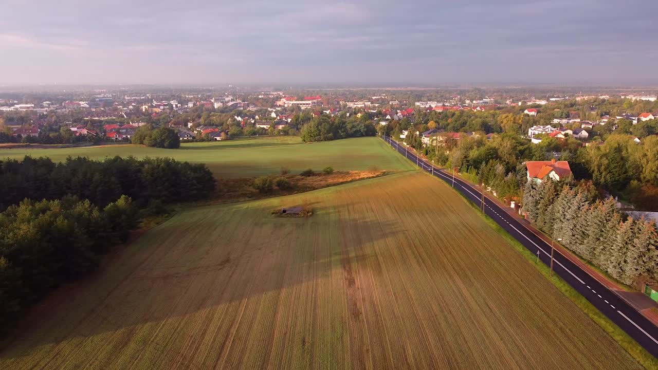 교외 주택에서 도로로 분리된 들판 위로 우거진 숲 뒤에서 솟아 오르고 비가 내린 직후 잎이 무성한 교외와 먼 도시를 위에서 바라보고 있습니다.