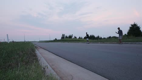 wide static shot of friend recording a male skateboarder failing a skateboard trick on an empty road.