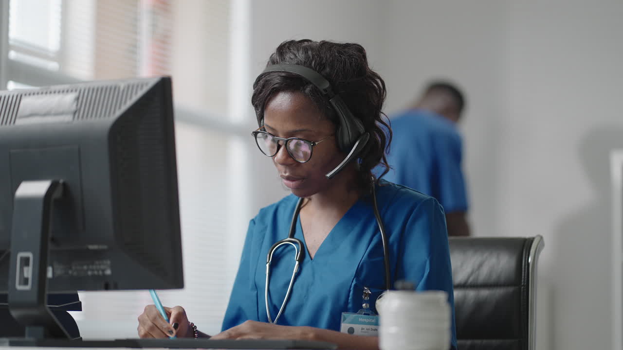 African Female medical assistant wears white coat headset video calling distant patient on computer. Doctor talking to client using virtual chat computer app. Telemedicine remote healthcare