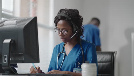 asistente médica africana usa casco blanco auriculares llamando a un paciente distante por computadora. médico hablando con el cliente usando una aplicación de computadora de chat virtual. telemedicina atención médica remota